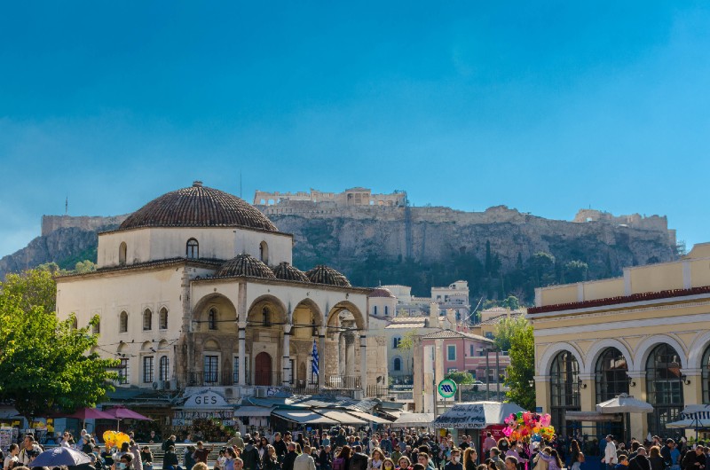 Monastiraki Square in Athens with markets, Tzistarakis Mosque, and Acropolis in the background on a sunny day.