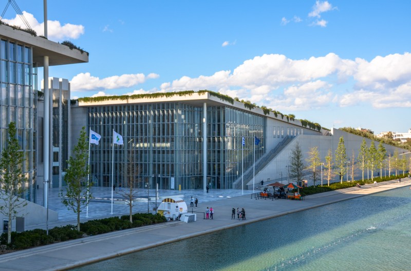 Exterior view of the Stavros Niarchos Foundation Cultural Center in Athens with glass facade, canal, and people walking