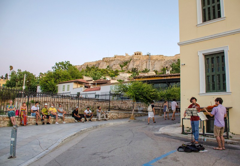 How to Get to Plaka in Athens - Plaka street in Athens with street musicians and the Acropolis in the background.