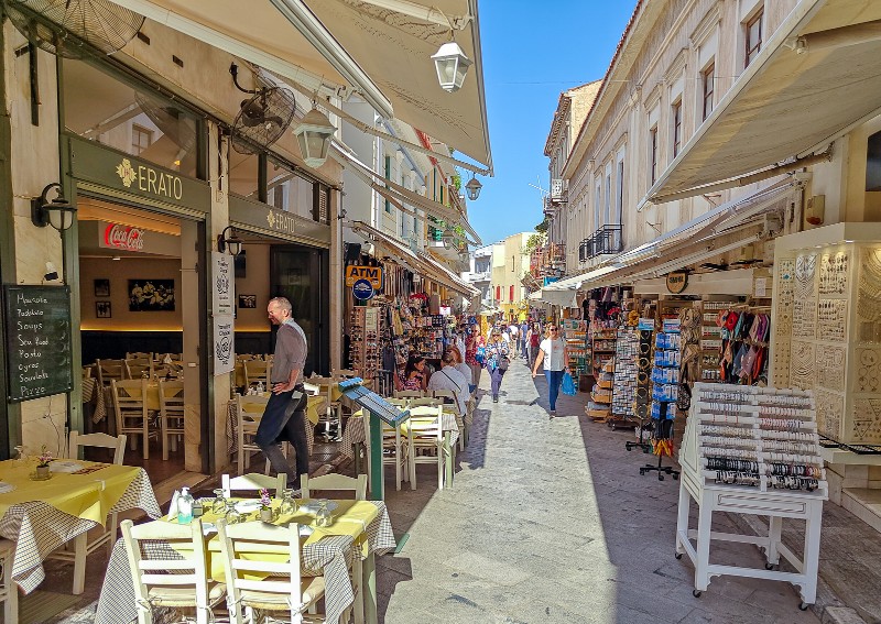 Where to stay in Plaka district - Narrow pedestrian street in Plaka Athens lined with outdoor cafés and souvenir shops, showing the atmosphere of staying in the neighborhood.