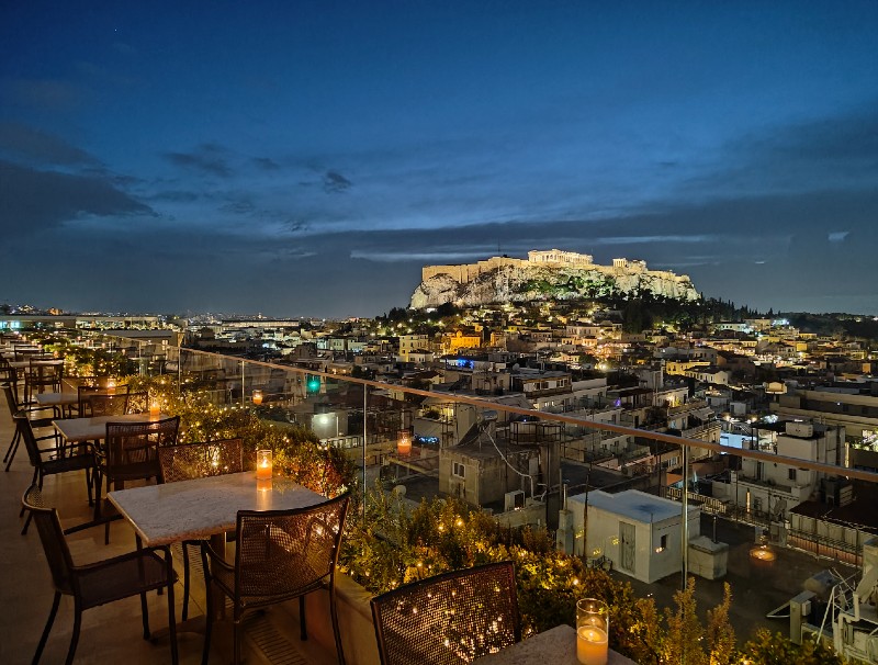 Rooftop bar in Athens at night with candlelit tables and a panoramic view of the illuminated Acropolis.