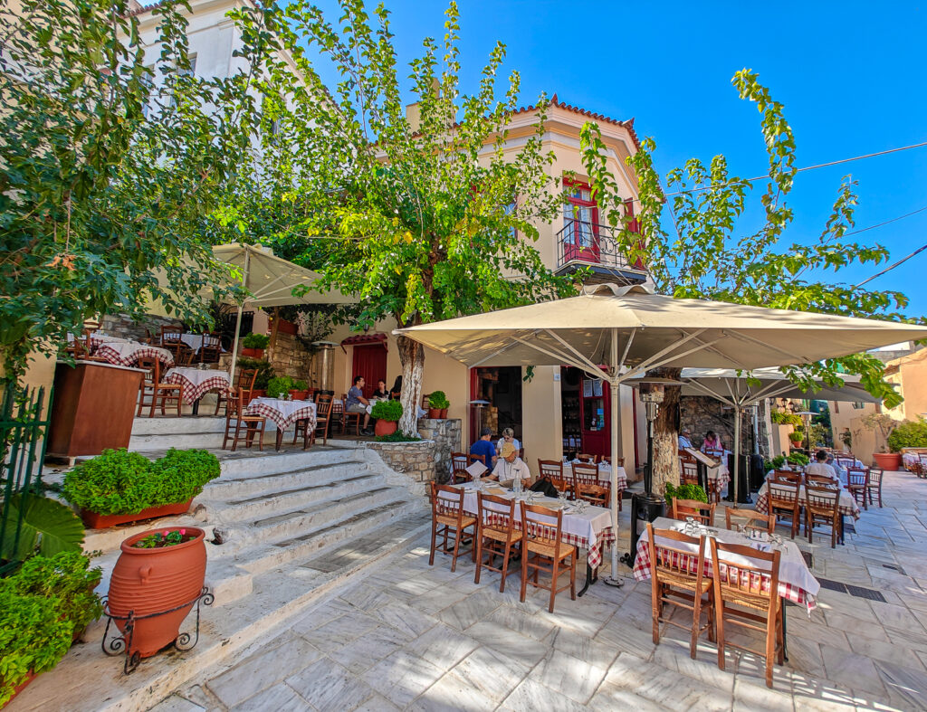 where to eat in Plaka - Colorful outdoor seating at Psaras Taverna in Plaka, Athens, with red and green chairs under umbrellas along a cobblestone street