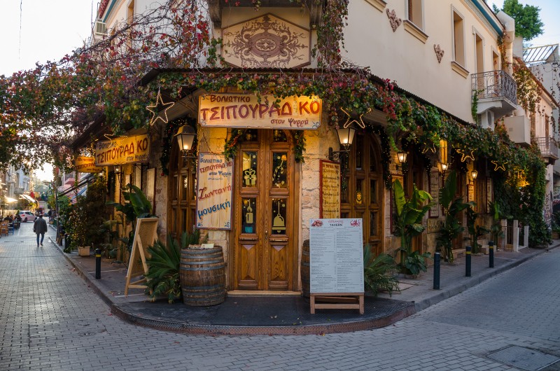 restaurants in Psirri district - Corner view of a traditional tsipouradiko in Psirri, Athens, with ivy-covered walls, wooden doors, and warm evening lights