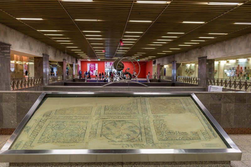 Ancient mosaic displayed inside Syntagma metro station in Athens, surrounded by modern architecture and commuters.